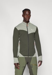 Veste zippée verte et grise avec un motif en maille texturé, col haut et détails de fermeture éclair orange contrastants. Présente une coupe ajustée.