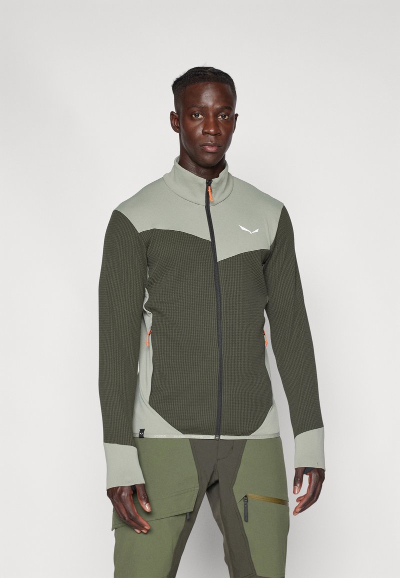 Veste zippée verte et grise avec un motif en maille texturé, col haut et détails de fermeture éclair orange contrastants. Présente une coupe ajustée.