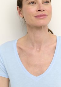 Jasnoniebieska koszulka typu V-neck z krótkim rękawem, miękka w dotyku, dopasowany krój i przeszycia wokół dekoltu.