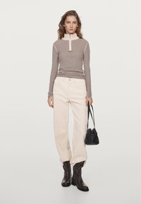 Gestreiftes Langarmshirt in Braun und Creme, kombiniert mit cremefarbenen Hosen. Die Accessoires umfassen eine kleine schwarze Handtasche und braune kniehohe Stiefel.