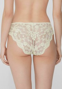 Culottes en dentelle jaune pâle avec des motifs floraux, des bords festonnés et une texture translucide, conçues pour une silhouette ajustée et près du corps.