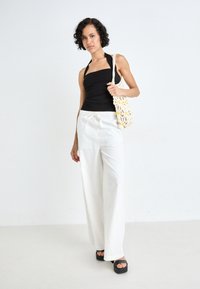 Black halter top paired with white wide-leg pants, held with a drawstring. Accessories include a crocheted bag with flower details and platform sandals.