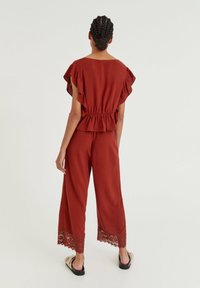 Rode peplumtop met ruffle-mouwen, gecombineerd met wijde broek met kantafwerking aan de zoom. Gemaakt van een lichtgewicht stof.