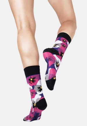Farverige sokker med blomster mønstre i pink, lilla og sort. De har en sort manchet og en blød tekstur, perfekt til komfort.