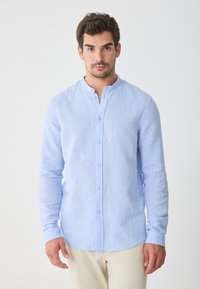 Light blue long-sleeve shirt with a mandarin collar, front button closure, and a subtle textured fabric. Tailored fit, straight hem.