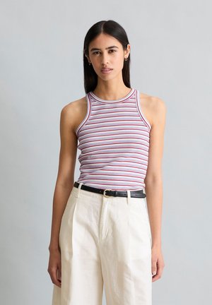 Jeune femme portant un haut sans manches rayé rouge et blanc, un pantalon blanc taille haute et une ceinture noire sur fond gris uni.