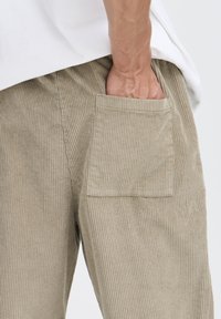 Beige corduroy pants with a textured ribbed surface, featuring a patch pocket on the back and a relaxed fit.