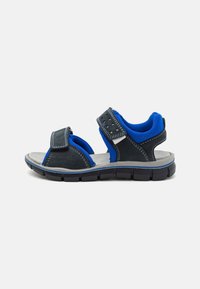 Schwarze und blaue Sandale mit verstellbaren Riemen, einem strukturierten Fußbett und einer stabilen Gummisohle mit einem Profilmuster für besseren Halt.