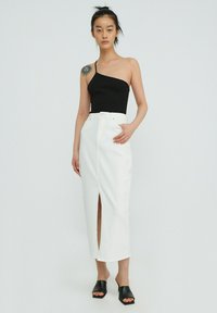 Zwarte one-shoulder top, witte denimrok met een voorknop, en zwarte hoge muiltjes. Minimalistisch ontwerp, gladde textuur en aansluitende silhouet.