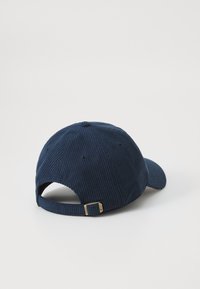 Marineblauwe corduroy pet met een gebogen rand, ribbelstructuur en een verstelbare band met een gouden metalen gesp aan de achterkant.