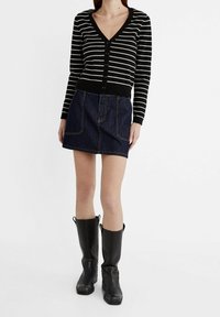 Zwart-witte gestreepte cardigan met een V-hals en knopen, gecombineerd met een donkerdenim minirok met voorzakken en kniehoge zwarte laarzen.