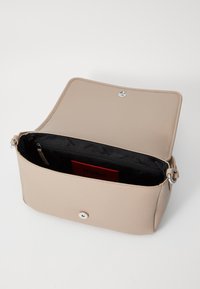Beige skinnveske med magnetlås, som har et innvendig glidelomme og en svart foring med et "HUGO"-mønster.