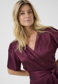 Burgundy wrap-around dress made of textured fabric, featuring short sleeves, a deep V-neck, and a waist tie for a fitted silhouette.