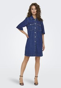 Denim shirt dress in dark blue, featuring a collared neck, short sleeves, front button closure, and two chest pockets. Smooth texture.