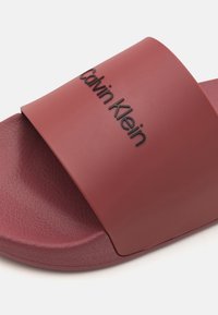 Sandale pe plajă Calvin Klein de culoare burgundă mată, având o curea lată cu un finisaj texturat și un logo embosat, talpă moale pentru confort.