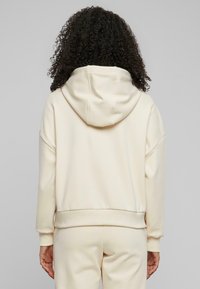 Sweatshirt à capuche de couleur crème avec une coupe décontractée, des poignets et un ourlet côtelés, présentant un tissu doux et un design minimaliste.