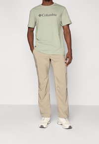Svetle zelené tričko s krátkým rukávem s logem "Columbia", doplněné béžovými cargo kalhotami a bílými teniskami. Pohodlný a funkční outfit.