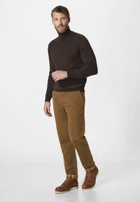 Brauner Rollkragenpullover, beige Chinos und braune Schnürstiefel mit karierten Säumen. Weicher Stoff und taillierte Passform, die klare Linien betont.