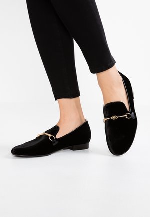 Sorte fløjls-loafers med spids tå og lille hæl. Har guldfarvede metalaccenter og et dekorativt rem-detalje.