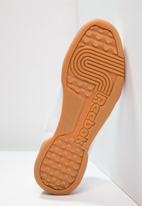 Sole di sneaker bianca con una suola in gomma naturale testurizzata che presenta motivi a onda e linee, contrassegnata con il marchio "Reebok" in lettere bold.
