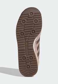 Hnědá gumová podrážka tenisky s texturovaným vzorem proti skluzu, obsahující kruhové důlky a tři tmavé pruhy. Na boku je viditelné logo "adidas".