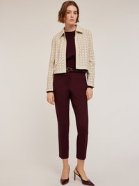 Veste perforée beige raccourcie sur un top bordeaux, associée à un pantalon bordeaux ajusté et des escarpins bourgogne à talon.