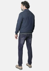 Sudadera azul marino con cuello alto, puños y cinturilla acanalados; combinada con vaqueros desgastados de color azul y zapatos beige. Vista trasera de la ropa.