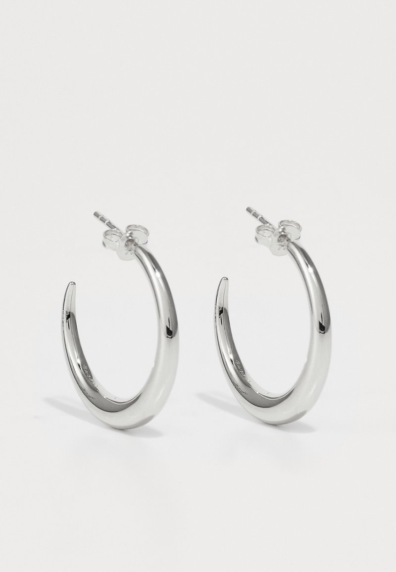 Silberne Creolen mit einer glatten, polierten Oberfläche, die ein geschwungenes Design und einen sicheren Verschluss aufweisen. Hergestellt aus Metall mit einer reflektierenden Oberfläche.