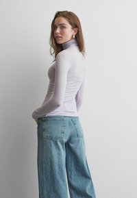 Haut col roulé à manches longues de couleur violet clair, coupe ajustée, associé à un jean large à teinte moyenne avec des poches arrière.