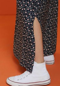 Vestido maxi floral azul marino con una abertura lateral, combinado con zapatillas deportivas blancas de caña alta. La tela tiene un aspecto texturizado con pequeños patrones floralescoloridos.