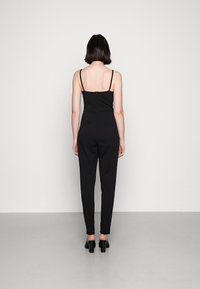 Svart jumpsuit med tunna axelband, figurnära design, smalnande ben och dragkedjestängning i ryggen, tillverkad av slätt tyg.