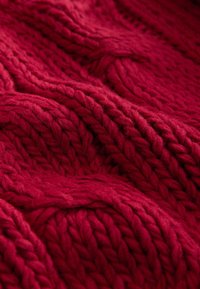 Red knitted fabric featuring thick, textured yarn in a cable pattern. The surface is soft with visible stitching and depth.