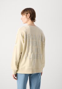Felpa di colore crema con una vestibilità rilassata, caratterizzata da grandi lettere grigie in rilievo sul retro che recitano "PERCHÉ NON C'È UN PIANETA B."