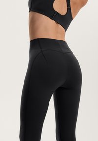 Czarne legginsy z wysokim stanem o bezszwowym designie, z teksturowanymi detalami szwów i gładkim, rozciągliwym materiałem.