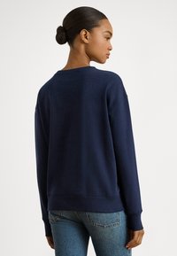 Φούτερ σε ναυτικό μπλε με στρογγυλή λαιμόκοψη, μακριά μανίκια και ριμπ μανσέτες. Λεία υφή και άνετη εφαρμογή· η πίσω όψη αποκαλύπτει την απλότητα στο σχέδιο.