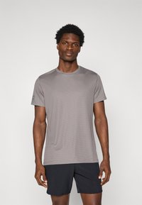 Grå atletisk t-shirt med korte ærmer og rund hals, der har en subtil tekstur og et logo-accent på venstre ærme.