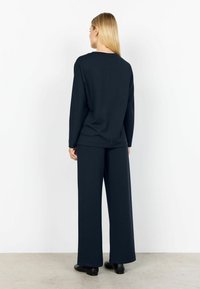 Marineblauer Pullover mit Rundhalsausschnitt, langen Ärmeln und einer Rückennaht, kombiniert mit weiten Hose. Beide Teile sind aus weichem, strukturiertem Stoff gefertigt.