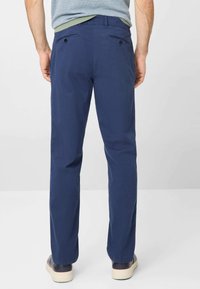 Blauwe katoenen broek heeft een recht gesneden pijp, knoopzakken aan de achterkant en een gladde textuur, gecombineerd met donkere schoenen en een gestreept shirt.