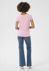 Camiseta rosa de manga corta con escote en forma de barco, combinada con jeans acampanados azules y tacones blancos. Tejido de algodón, textura suave, estilo casual.