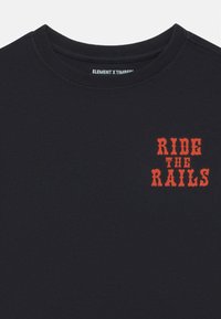 Čierne bavlnené tričko s okrúhlym výstrihom a červeným grafickým textom „RIDE THE RAILS“ na ľavej strane hrude. Mäkký materiál, voľný strih.