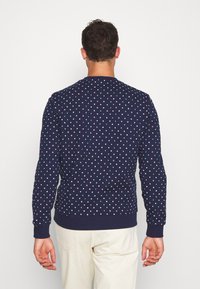 Felpa blu navy con pois bianchi e turchesi, scollo rotondo, polsini e orlo a costine, silhouette aderente.