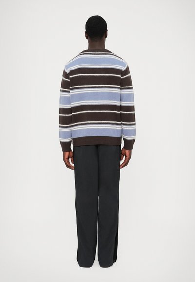 Pull en tricot avec des rayures horizontales bleu et marron, présentant un col rond et des manches longues, associé à un pantalon noir à jambes larges.