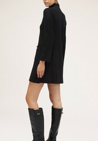 �Černé šaty po kolena s vysokým límcem, dlouhými rukávy a kapsou. Stylizované s černými kozačkami po kolena se zlatým akcentem.