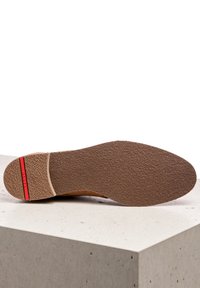 Suela marrón con superficie texturada, que presenta un acento rojo en el talón y un diseño liso y minimalista. Adecuada para varios estilos de calzado.