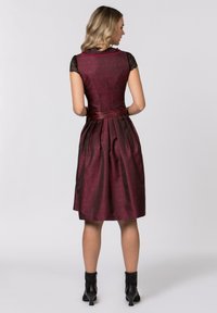 Burgundy dress with lace cap sleeves, fitted bodice, pleated skirt, and a satin belt. Textured floral pattern throughout. Black ankle boots.