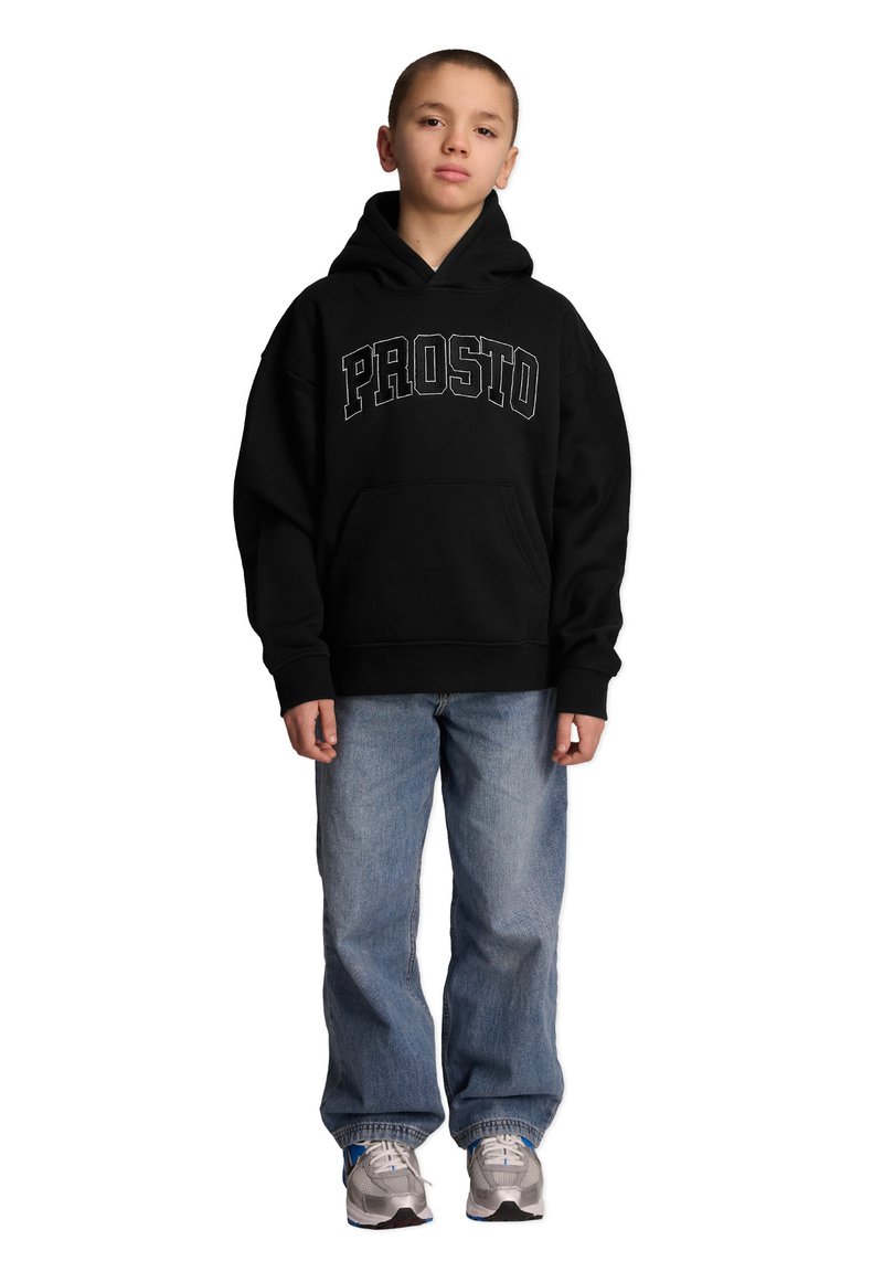 Czarna bluza z kapturem z napisem "PROSTO" w białych literach, zestawiona z luźnymi jasnoniebieskimi dżinsami i srebrnymi butami sportowymi.