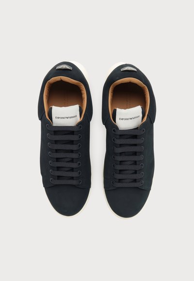 Paire de baskets noires à lacets avec semelles blanches et doublure intérieure marron, avec le logo Emporio Armani sur les étiquettes blanches de la languette.
