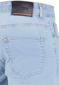 Jeans de mezclilla azul claro con una etiqueta de cuero negra, que cuentan con dos bolsillos traseros y costuras en contraste. Diseño sencillo y clásico.