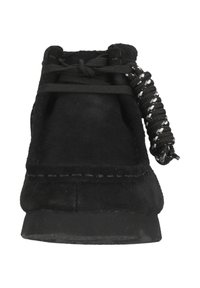 Svart mockaskinnsmoccasin med tjock sula och svarta snören knutna i en rosett, sedd framifrån mot en vit bakgrund.