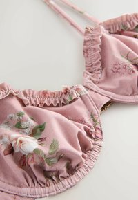 Soutien-gorge rose à armatures avec bordures froncées et fines bretelles réglables sur un fond clair.